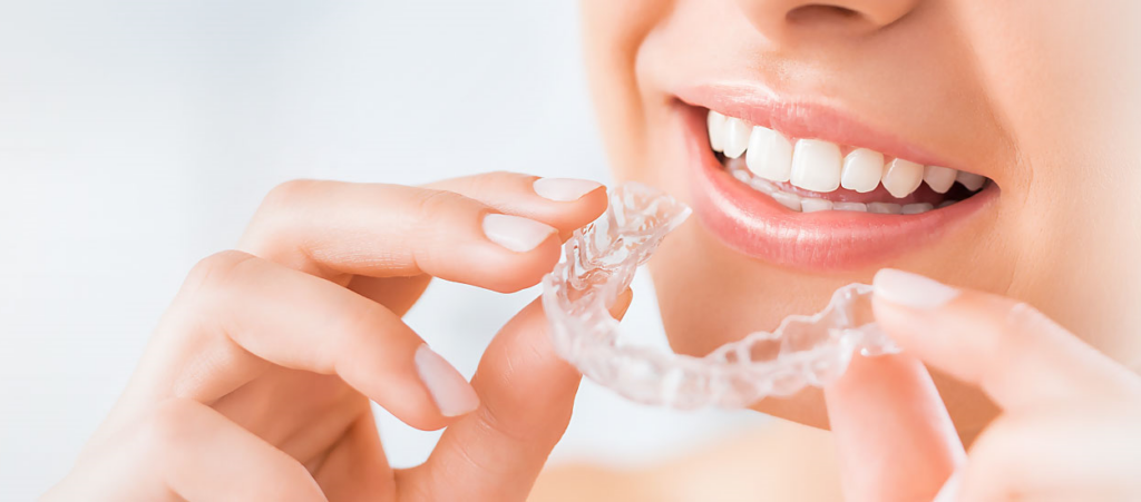 Woman holding Invisalign aligner near her mouth, showcasing clear orthodontic treatment for a straighter smile, relevant to cosmetic dentistry and spring Invisalign consultations.